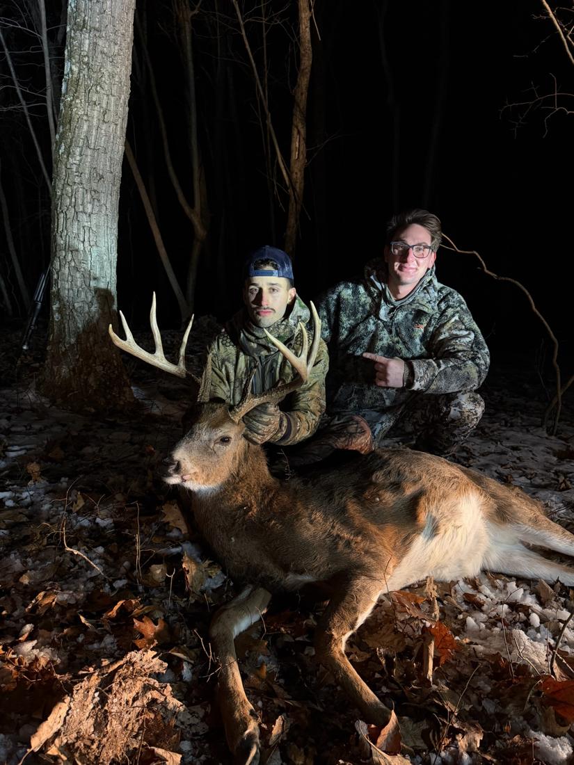 Two hunters with a whitetail buck at night, snow on the ground